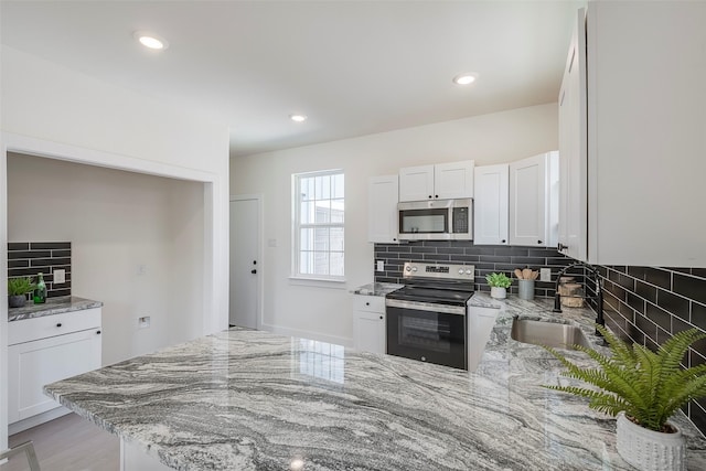 kitchen with light stone counters, white cabinetry, sink, and appliances with stainless steel finishes