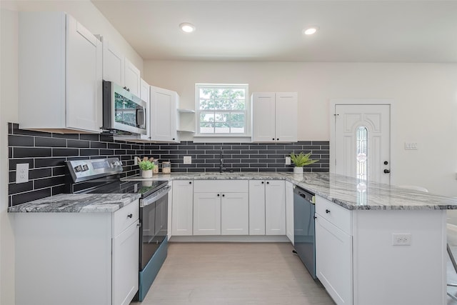 kitchen with decorative backsplash, kitchen peninsula, light stone countertops, stainless steel appliances, and white cabinets