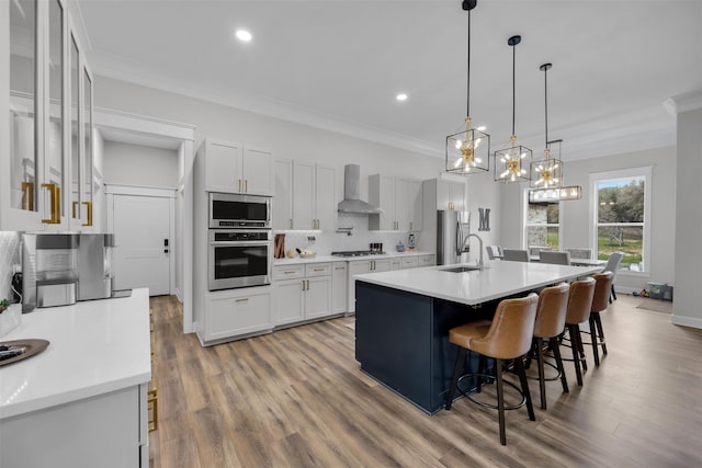 kitchen featuring white cabinets, appliances with stainless steel finishes, a kitchen island with sink, and wall chimney range hood