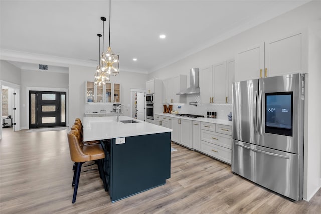 kitchen with wall chimney exhaust hood, appliances with stainless steel finishes, a kitchen breakfast bar, a kitchen island with sink, and white cabinets