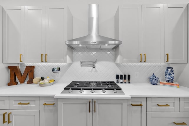 kitchen featuring white cabinets, stainless steel gas stovetop, decorative backsplash, and wall chimney range hood