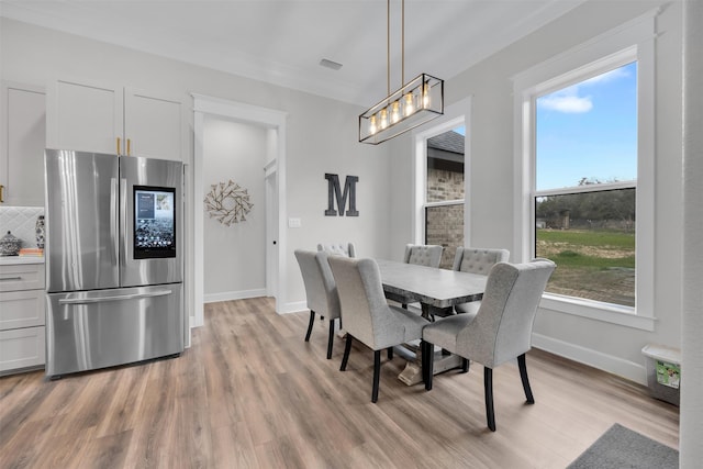 dining area featuring light wood-type flooring and crown molding