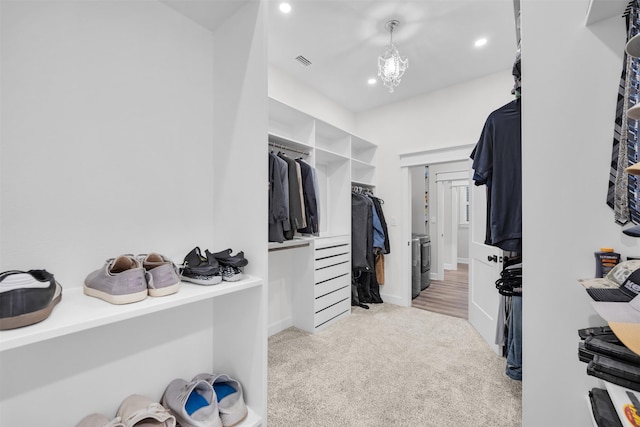 spacious closet with washer / dryer, light colored carpet, and an inviting chandelier