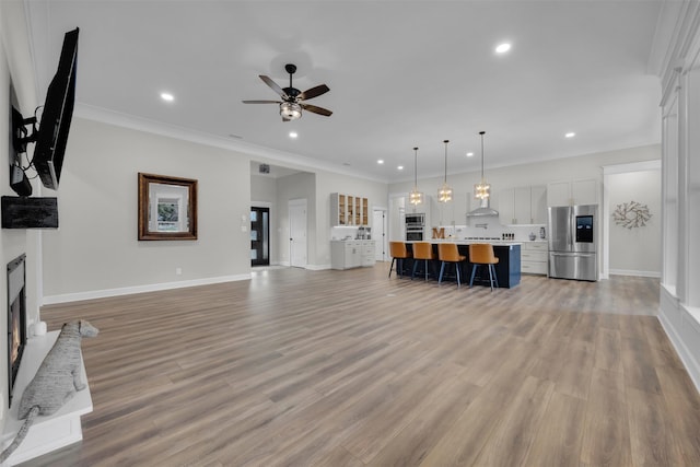 unfurnished living room with ceiling fan, ornamental molding, and light wood-type flooring