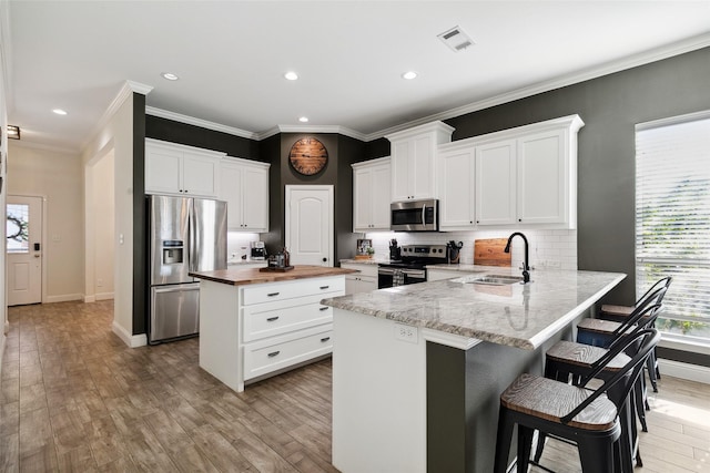 kitchen with sink, a breakfast bar area, white cabinetry, appliances with stainless steel finishes, and kitchen peninsula