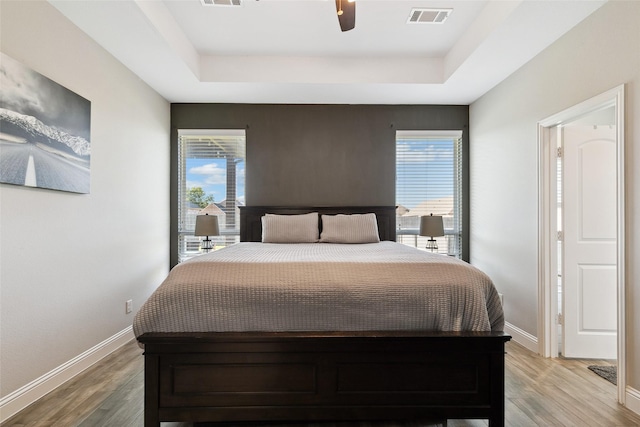 bedroom with multiple windows, hardwood / wood-style floors, a raised ceiling, and ceiling fan