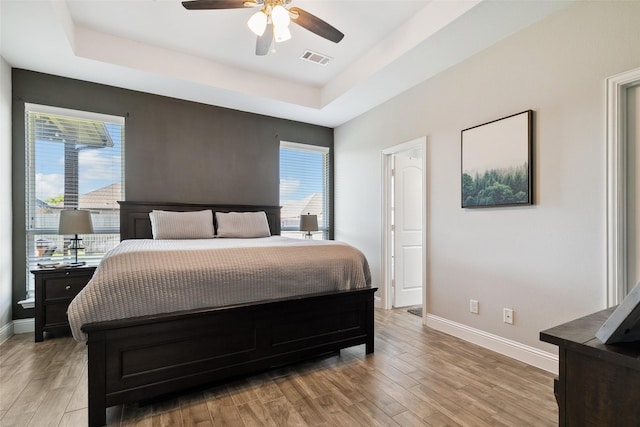 bedroom featuring ceiling fan, light wood-type flooring, and a tray ceiling