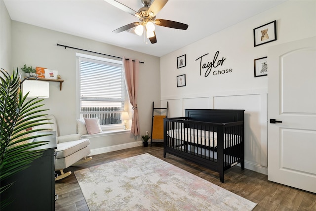 bedroom featuring dark hardwood / wood-style flooring, a nursery area, and ceiling fan