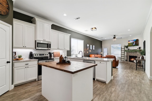 kitchen with a kitchen island, butcher block countertops, white cabinets, kitchen peninsula, and stainless steel appliances