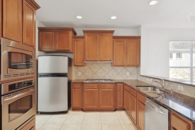 kitchen with appliances with stainless steel finishes, backsplash, sink, light tile patterned floors, and dark stone countertops