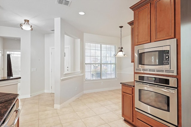 kitchen with decorative light fixtures, light tile patterned floors, stainless steel appliances, and dark stone counters