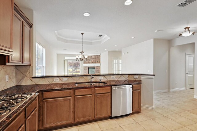 kitchen with appliances with stainless steel finishes, a raised ceiling, sink, a notable chandelier, and dark stone countertops