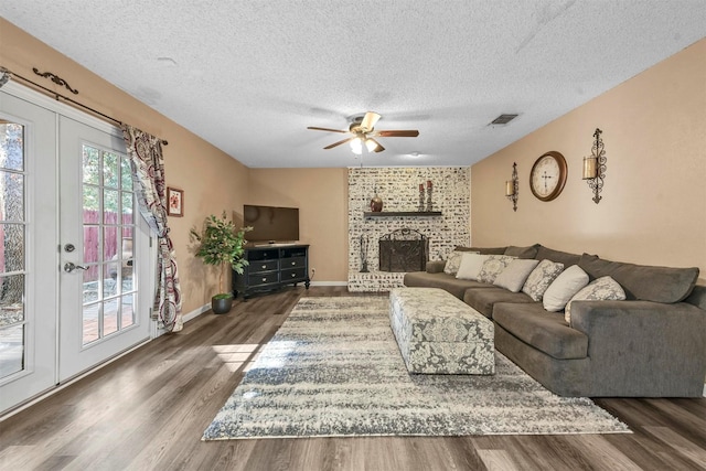 living area featuring dark wood finished floors, visible vents, a brick fireplace, ceiling fan, and a textured ceiling