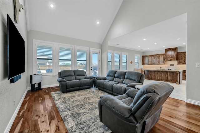 living room featuring ornamental molding, sink, high vaulted ceiling, and light wood-type flooring