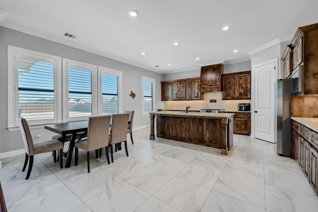 kitchen featuring backsplash, a kitchen island with sink, stainless steel appliances, crown molding, and dark brown cabinets