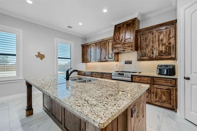 kitchen featuring light stone countertops, backsplash, sink, stainless steel range oven, and an island with sink