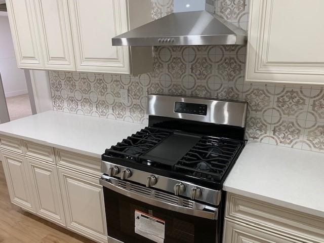 kitchen with backsplash, wall chimney exhaust hood, light hardwood / wood-style floors, and stainless steel gas range