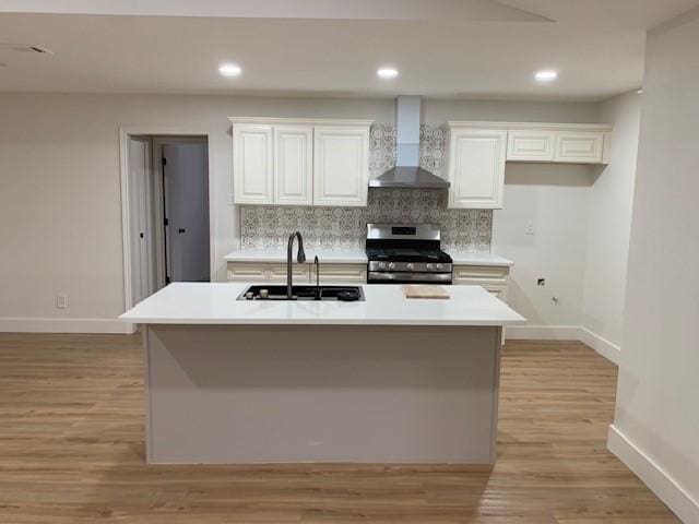 kitchen featuring sink, wall chimney exhaust hood, stainless steel gas stove, an island with sink, and tasteful backsplash