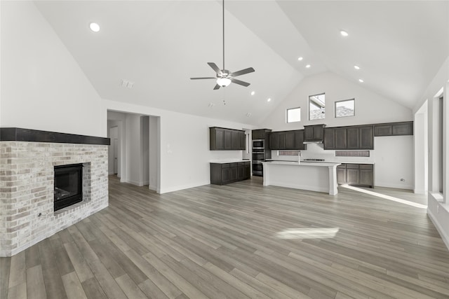 unfurnished living room with ceiling fan, a fireplace, high vaulted ceiling, and light wood-type flooring