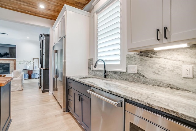 kitchen with white cabinets, sink, appliances with stainless steel finishes, light stone counters, and wood ceiling