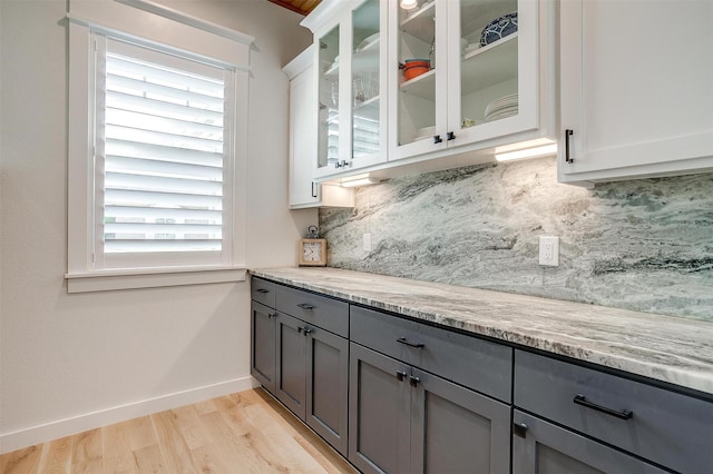 kitchen featuring white cabinets, light stone counters, light wood-type flooring, and backsplash