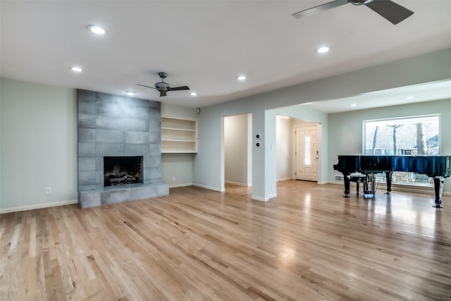 unfurnished living room with built in shelves, ceiling fan, a tile fireplace, and light hardwood / wood-style flooring