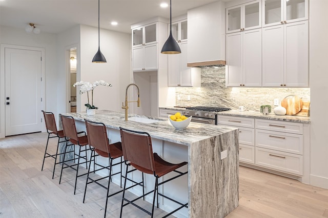 kitchen with decorative light fixtures, light stone counters, white cabinetry, and a kitchen island with sink