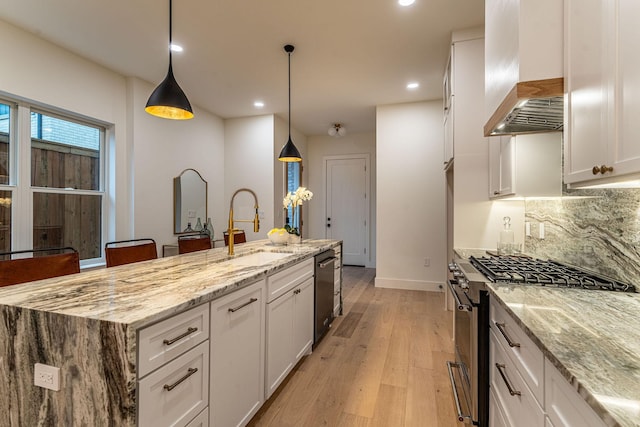 kitchen featuring pendant lighting, wall chimney range hood, sink, white cabinetry, and stainless steel appliances