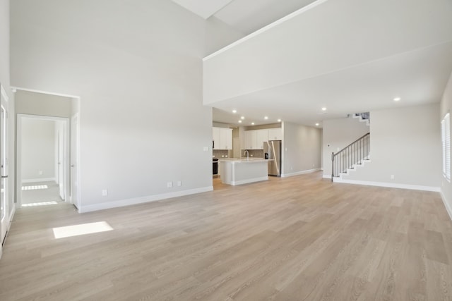 unfurnished living room featuring light wood-type flooring, a high ceiling, and sink