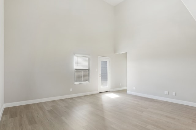 empty room with light wood-type flooring and a towering ceiling