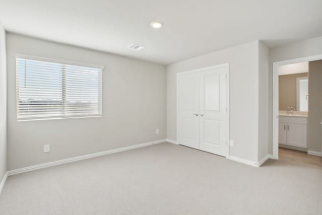 unfurnished bedroom featuring a closet, sink, light colored carpet, and ensuite bath