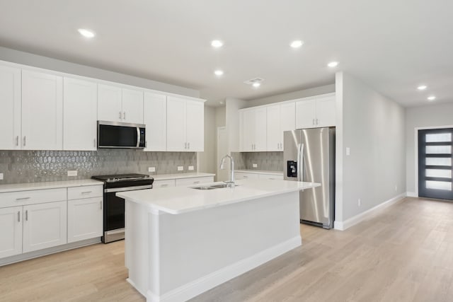 kitchen with an island with sink, appliances with stainless steel finishes, light wood-type flooring, white cabinets, and sink