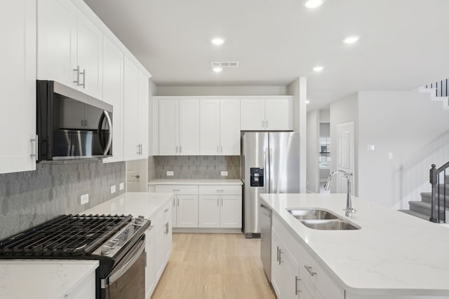 kitchen featuring light stone countertops, white cabinetry, stainless steel appliances, sink, and a kitchen island with sink