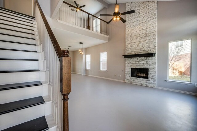 stairway with concrete flooring, ceiling fan, beam ceiling, high vaulted ceiling, and a fireplace