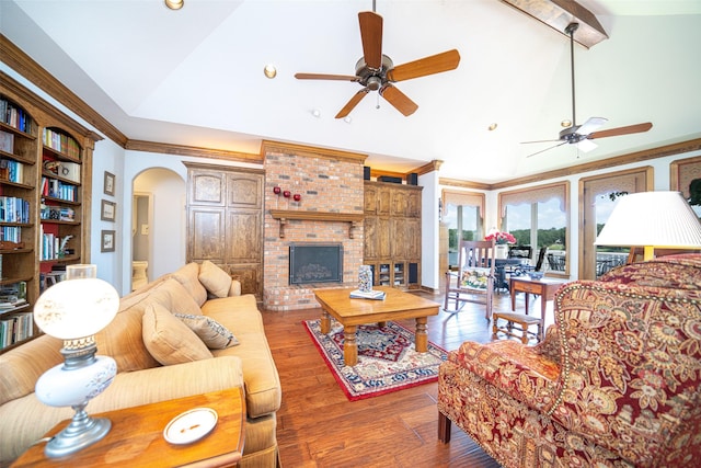 living room featuring vaulted ceiling, wood-type flooring, ornamental molding, ceiling fan, and a brick fireplace