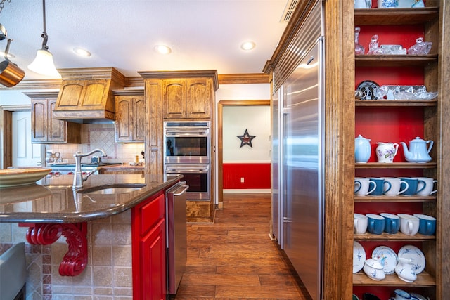 kitchen with premium range hood, hanging light fixtures, dark hardwood / wood-style flooring, stainless steel appliances, and backsplash