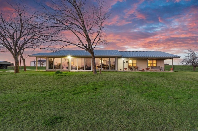 back house at dusk with a patio area and a lawn