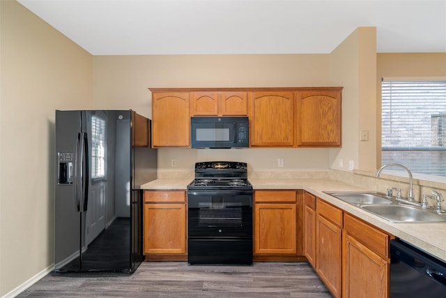 kitchen with black appliances, wood finished floors, a sink, and light countertops