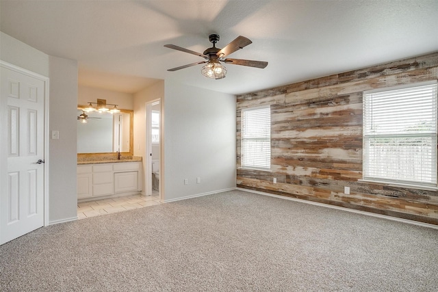 unfurnished bedroom with light carpet, connected bathroom, ceiling fan, and wooden walls