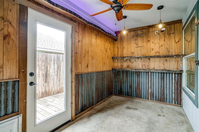 interior space with wooden walls, ceiling fan, and concrete floors