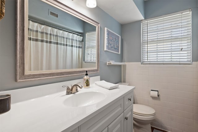 bathroom featuring vanity, tile walls, and toilet