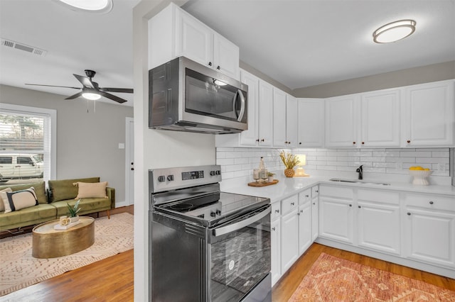 kitchen with appliances with stainless steel finishes, light wood-type flooring, tasteful backsplash, ceiling fan, and white cabinetry