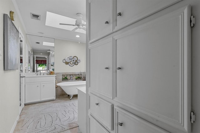 bathroom featuring a skylight, a bathtub, vanity, ceiling fan, and tile walls