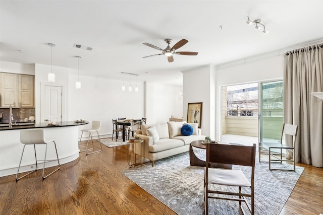 living room featuring wood-type flooring, ceiling fan, and sink