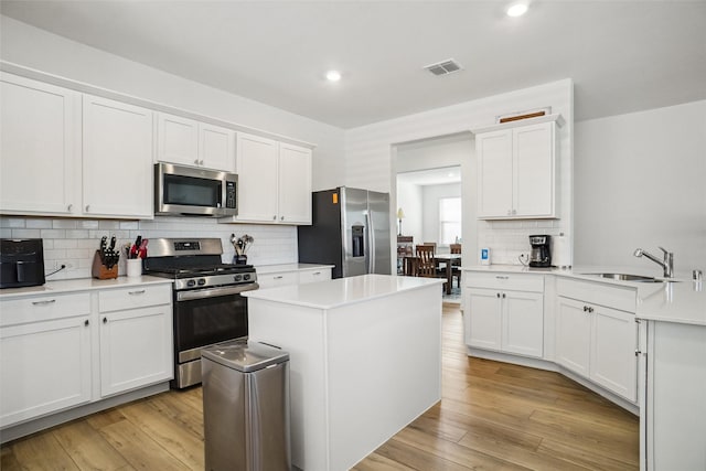 kitchen with sink, light hardwood / wood-style flooring, appliances with stainless steel finishes, a kitchen island, and white cabinetry