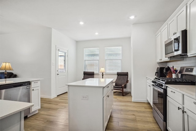 kitchen with a kitchen island, light hardwood / wood-style floors, decorative backsplash, white cabinets, and appliances with stainless steel finishes