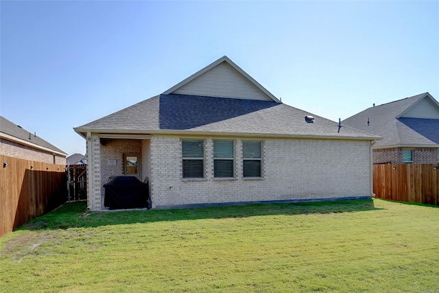 rear view of house with brick siding, a fenced backyard, a lawn, and roof with shingles