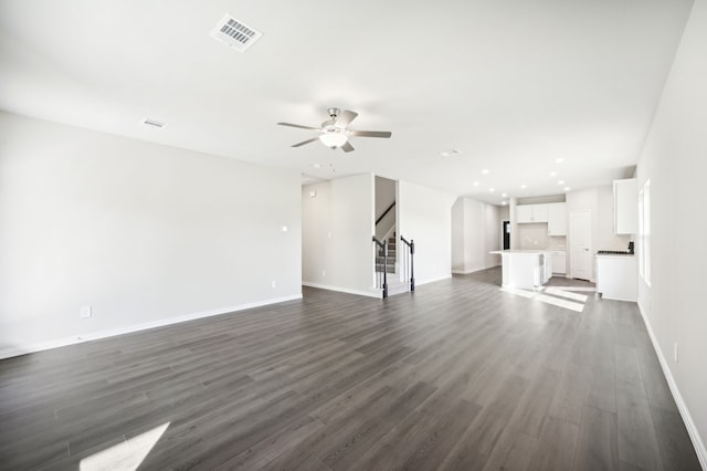 unfurnished living room with dark wood-style flooring, visible vents, ceiling fan, baseboards, and stairs