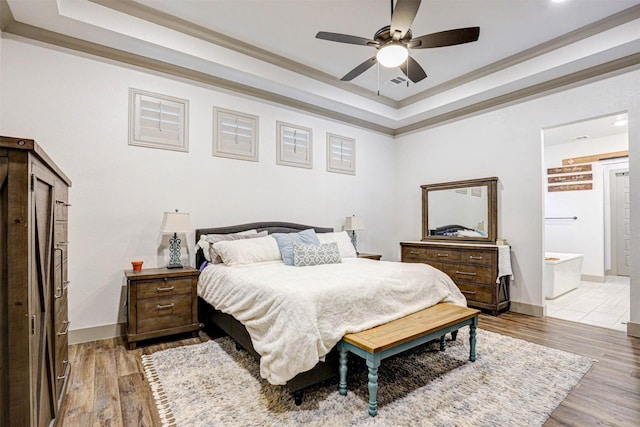 bedroom featuring crown molding, ensuite bath, ceiling fan, a tray ceiling, and wood-type flooring