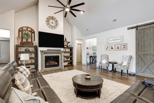 living room with hardwood / wood-style floors, a barn door, high vaulted ceiling, and ceiling fan